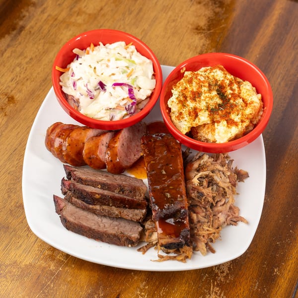 Barbecue platter with sliced sausage, brisket, rib, pulled pork, coleslaw, and potato salad.