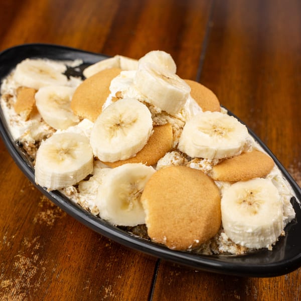Banana pudding with sliced bananas, vanilla wafers, and creamy topping in a black dish.