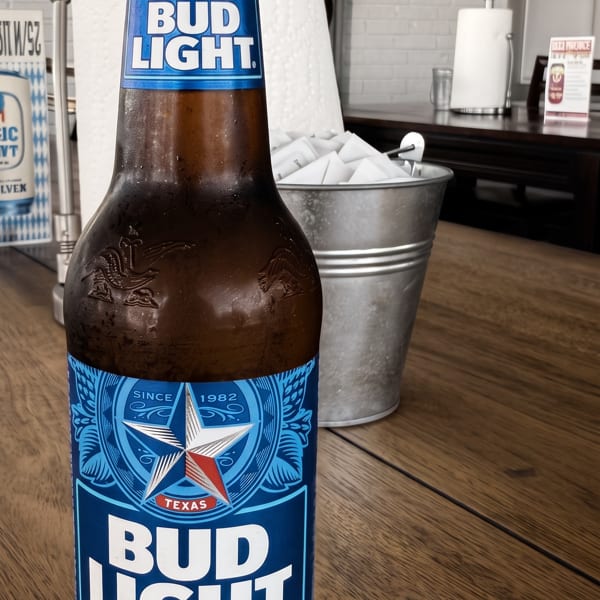 Cold Bud Light bottle on a wooden table with napkins and paper towels in the background.