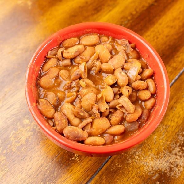Red bowl of savory beans in a rich sauce on a wooden table.