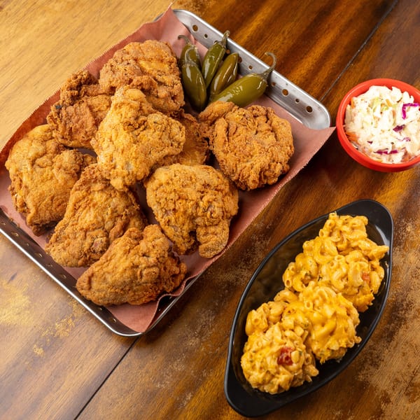 Fried chicken pieces with pickled jalapeños, coleslaw, and macaroni and cheese on a wooden table.