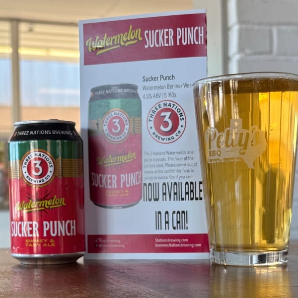Watermelon Sucker Punch beer can, promotional sign, and a glass of beer with Petty's BBQ logo.