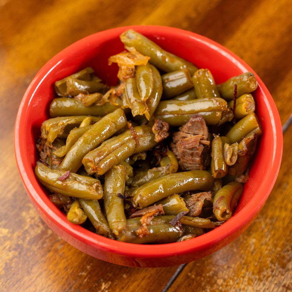 Red bowl filled with cooked green beans and shredded meat on a wooden table.