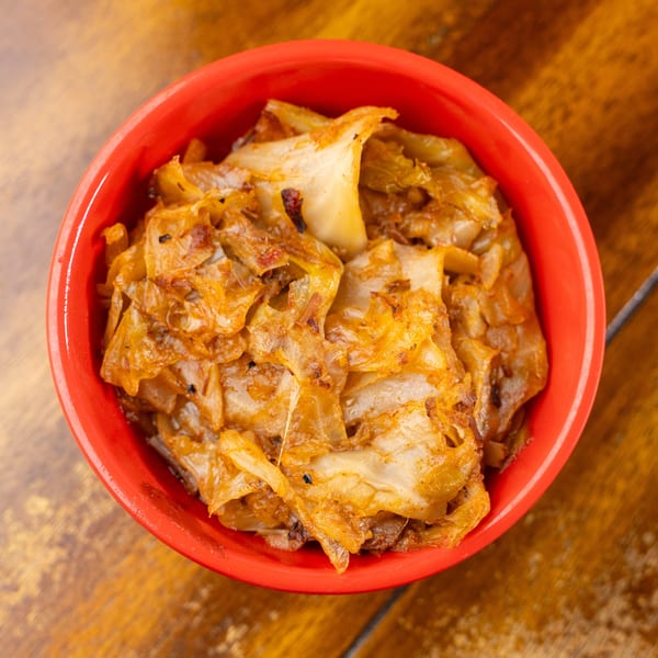 Golden-brown sautéed cabbage in a vibrant red bowl on a rustic wooden surface.