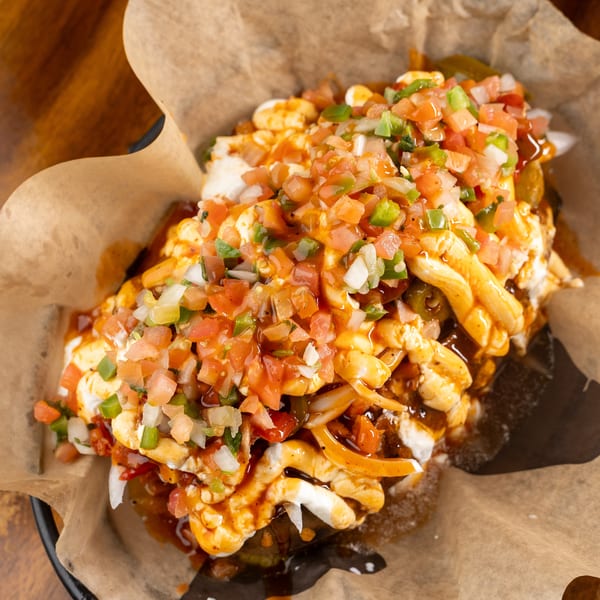 Loaded fries topped with melted cheese, fresh pico de gallo, and a savory sauce, served in paper.
