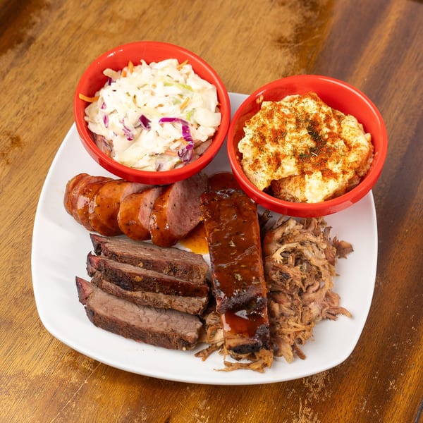 BBQ platter with sliced sausage, brisket, rib, pulled pork, coleslaw, and potato salad.